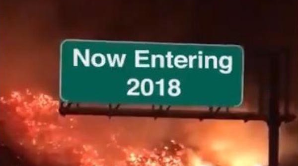 The words Now Entering 2018 are superimposed over a traffic sign. The photo is of a California highway surrounded by wildfires.